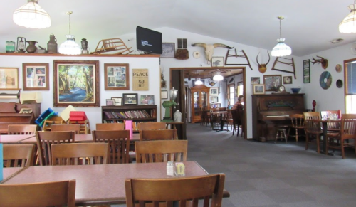 Cozy restaurant interior with wooden tables, chairs, and various wall decorations, including artwork and vintage items.