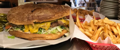 A large cheeseburger with lettuce, tomato, and pickles, served with a side of golden fries in a basket.