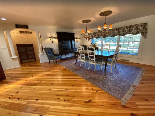 Bright dining room with a wooden table, white chairs, and large windows overlooking a scenic view, featuring hardwood floors.