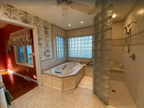 Spacious bathroom featuring a jacuzzi, glass block shower, and decorative wallpaper. Natural light from large windows.