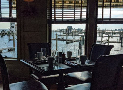 A dining table set for breakfast, with a view of a marina and water through large windows.
