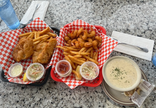 Two baskets of fried food with fries, shrimp, and dipping sauces, alongside a bowl of creamy soup on a table.