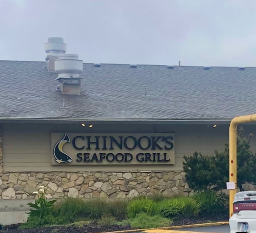 Sign for Chinook's Seafood Grill on a stone building, with a cloudy sky in the background.