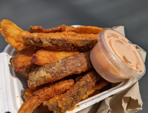 A container of crispy fried pickles served with a small cup of dipping sauce.