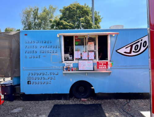 A blue food truck named Jojo offers sandwiches, fried potatoes, and fried chicken, with a menu displayed at the window.