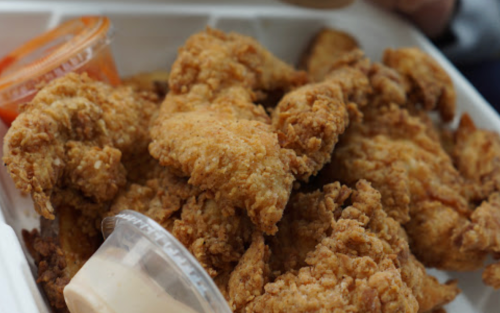 A close-up of crispy fried chicken pieces in a takeout container, with dipping sauces on the side.