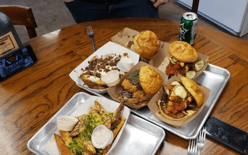 A table with various food items: two burgers, loaded fries, and dipping sauces, alongside a can of soda.