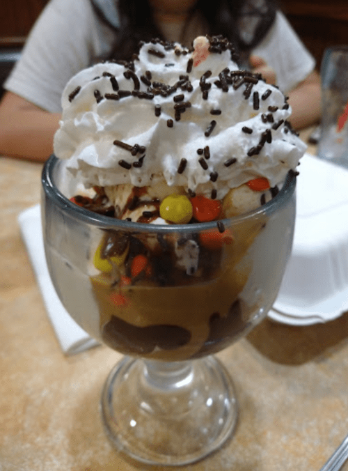 A delicious sundae in a glass, topped with whipped cream, chocolate sprinkles, and colorful candy pieces.