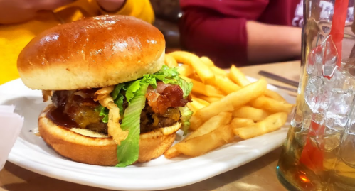 A juicy burger with lettuce, bacon, and sauce, served with crispy fries and a glass of iced tea.