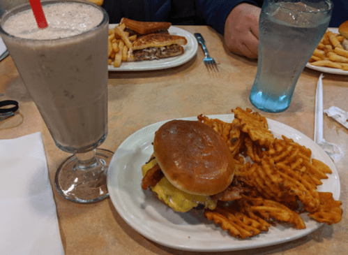 A plate with a cheeseburger, waffle fries, and a milkshake in a glass with a red straw.