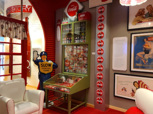 A retro Coca-Cola display featuring vintage bottles, memorabilia, and a "Slow School Zone" sign in a colorful room.