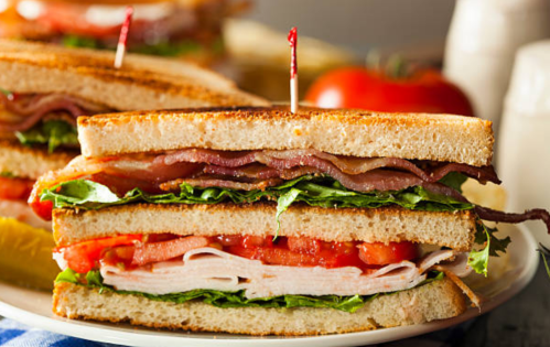 A close-up of a layered sandwich with turkey, bacon, lettuce, and tomato, served on toasted bread with a toothpick.