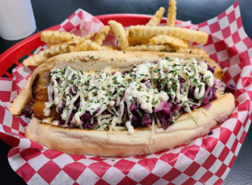 A hot dog topped with coleslaw and drizzled with sauce, served with crinkle-cut fries in a red-checkered basket.