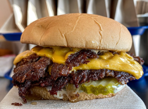 A close-up of a juicy burger with melted cheese, crispy beef, pickles, and a soft bun on a napkin.