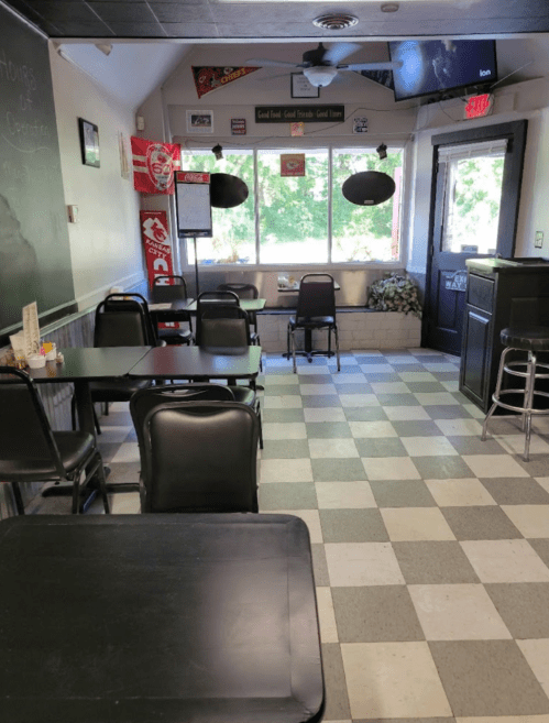 A cozy diner interior with black tables and chairs, checkered floor, and a window view of greenery outside.