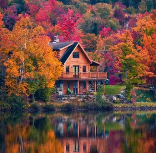 A cozy wooden cabin surrounded by vibrant autumn foliage, reflecting in a calm lake.
