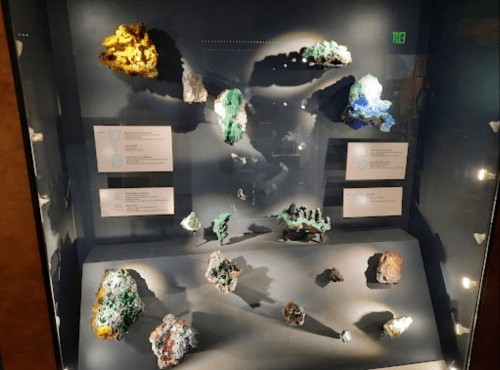Display case featuring various colorful mineral specimens with labels, illuminated for viewing.