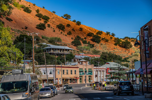 A scenic view of a small town with historic buildings, cars on the street, and a hillside in the background.
