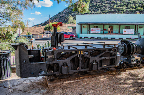 A vintage train engine on display outdoors, surrounded by desert vegetation and a mountainous backdrop.