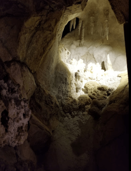 A dimly lit cave interior with stalactites and mineral formations illuminated by a soft light.