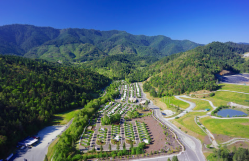 Aerial view of a lush green valley with a cluster of cabins and winding roads surrounded by mountains.