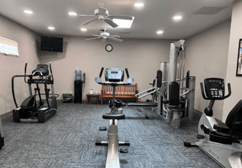 A small gym with exercise equipment, including treadmills, a stationary bike, and weight machines, in a well-lit room.