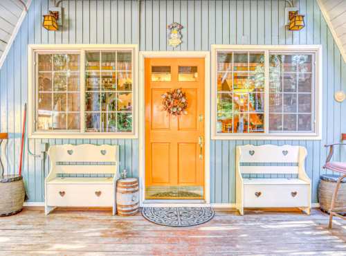 Charming entrance with an orange door, heart-shaped benches, and large windows surrounded by blue wooden siding.