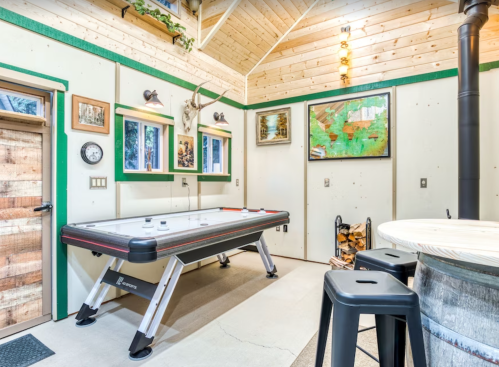 A cozy game room featuring an air hockey table, wooden decor, and a rustic bar area with stools.