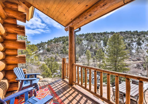 A wooden porch with blue chairs overlooks a scenic mountain landscape under a clear sky.