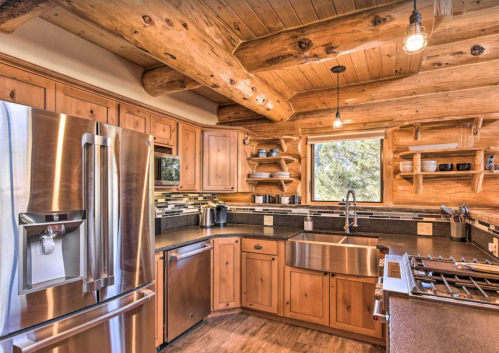 A rustic kitchen with wooden beams, stainless steel appliances, and a large window overlooking nature.