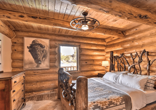 Cozy log cabin bedroom with rustic decor, featuring a large window and a bison portrait on the wall.