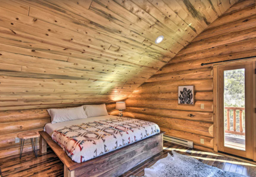 Cozy wooden bedroom with a sloped ceiling, a large bed, and a sliding door leading to a balcony.