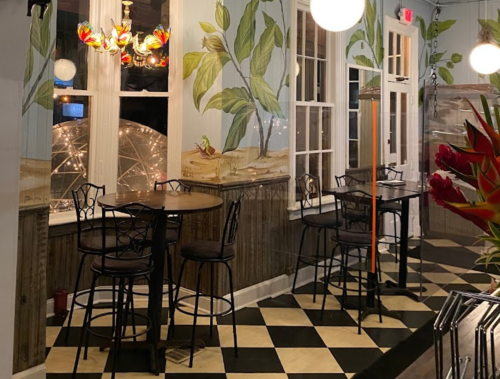 A cozy restaurant interior with checkered flooring, tall tables, and colorful wall murals featuring plants and birds.