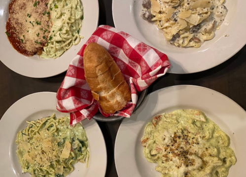 A table with five plates of pasta dishes and a bread roll in a red-checkered napkin.