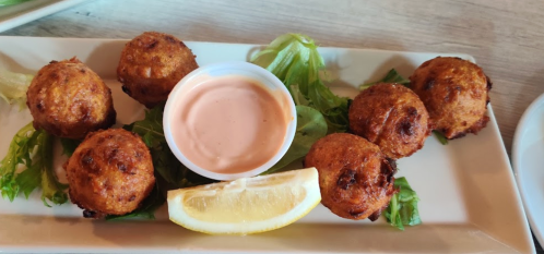 A plate of golden-brown fritters on lettuce, served with a dipping sauce and a lemon wedge.