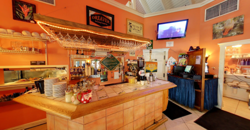 Cozy café interior with a wooden counter, coffee machines, and shelves of dishes against an orange wall.
