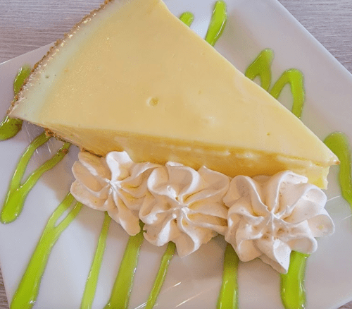 A slice of lemon pie topped with whipped cream, drizzled with green sauce on a white plate.