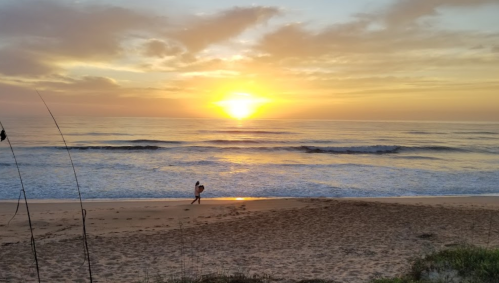 A serene beach at sunset, with gentle waves and a person walking along the shore.