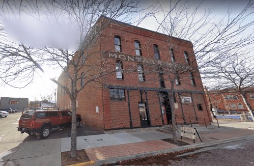A brick building with large windows and a sign reading "Mont" on a street corner, surrounded by bare trees.
