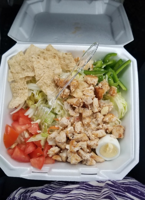 A takeout container filled with chopped chicken, lettuce, tomatoes, green peppers, and tortilla chips.