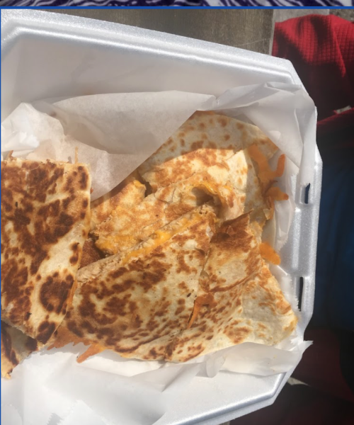 A takeout container filled with golden-brown quesadillas, partially cut and resting on white parchment paper.