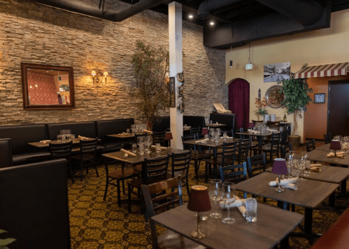 Cozy restaurant interior with stone walls, wooden tables, and elegant lighting, set for dining.