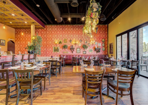 Cozy restaurant interior with wooden tables, chairs, and vibrant wall decor, featuring plants and framed pictures.