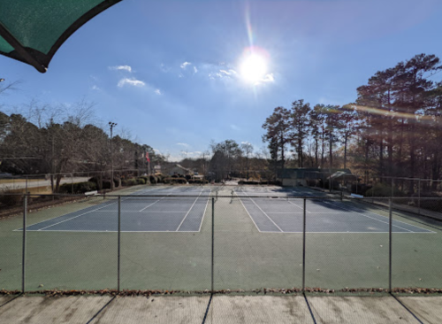 A sunny day at an empty tennis court surrounded by trees and a clear blue sky.