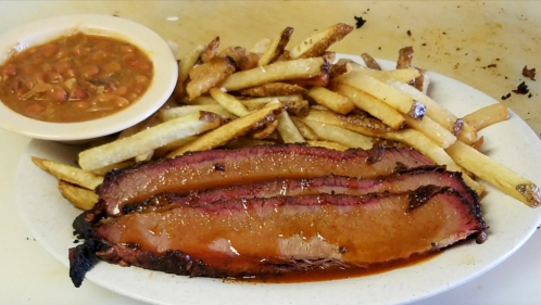 A plate with three slices of brisket, crispy fries, and a bowl of baked beans.