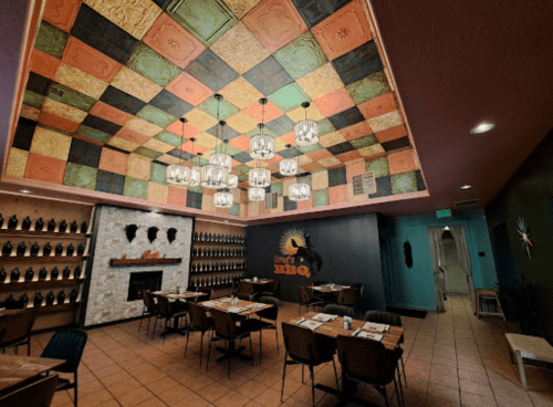 Interior of a BBQ restaurant featuring a colorful ceiling, wooden tables, and a cozy fireplace.