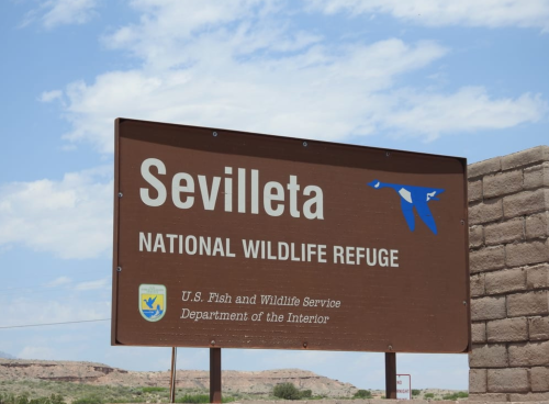 Sign for Sevilleta National Wildlife Refuge, featuring the U.S. Fish and Wildlife Service logo against a blue sky.