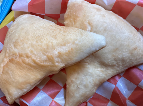 Two golden, fluffy fried pastries on a red and white checkered paper.