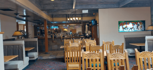 Interior of a restaurant featuring wooden tables, booths, and a bar area with colorful stained glass windows.