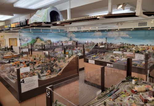 A detailed model train display featuring various landscapes, buildings, and trains in a museum setting.